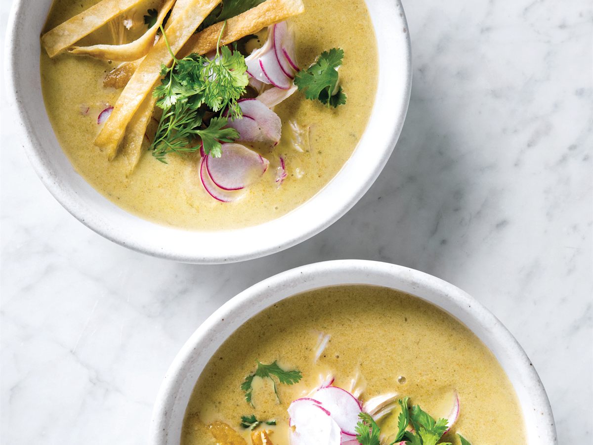 Two bowls of creamy chicken poblano soup topped with tortilla strips, sliced radishes, and cilantro